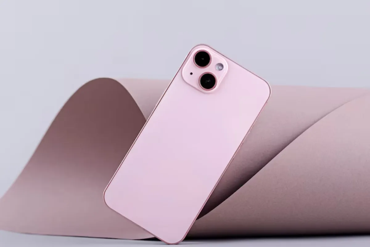 A pink smartphone resting on a curved piece of brown paper, showcasing its sleek design and dual camera features.