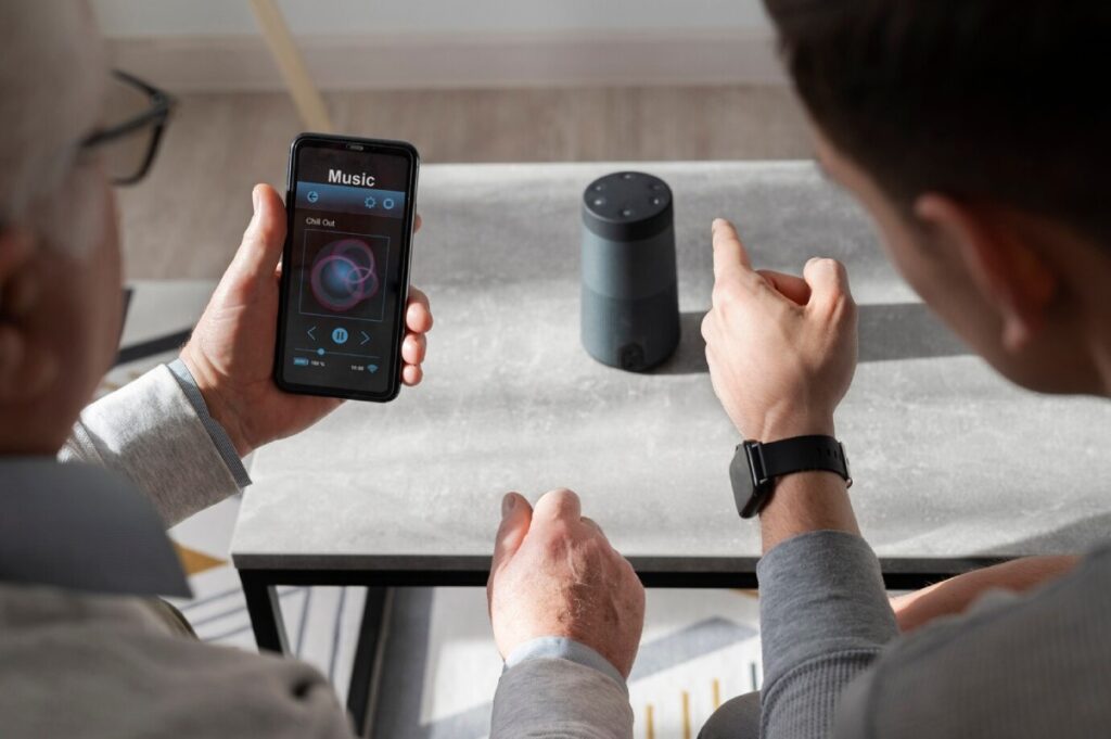 An older man and a younger man interactively discuss music while controlling a smart speaker using a smartphone.