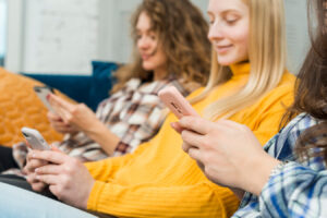 Three individuals sit closely together on a couch, each absorbed in their smartphones, surrounded by cozy decor.
