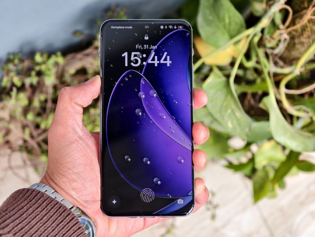 A person holding a smartphone displaying a vibrant lock screen with water droplets, set against green plants in the background.