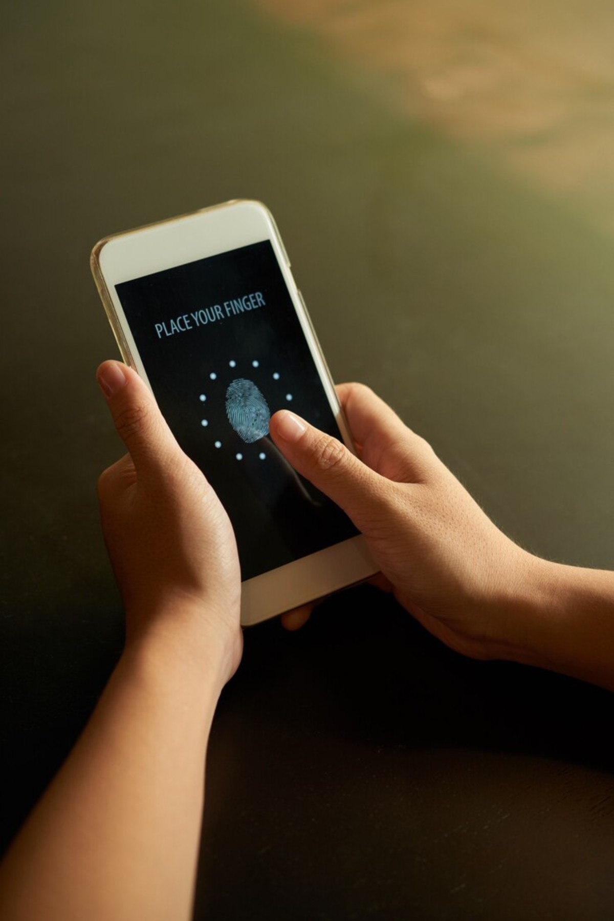 A person’s hands hold a smartphone displaying a fingerprint scanner with the text PLACE YOUR FINGER on the screen.