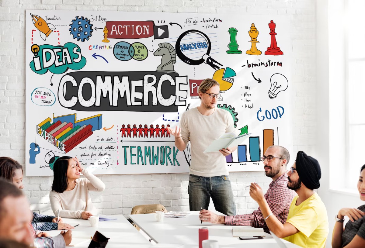 A presenter stands in front of a colorful brainstorming mural, discussing ideas about commerce with an attentive group.