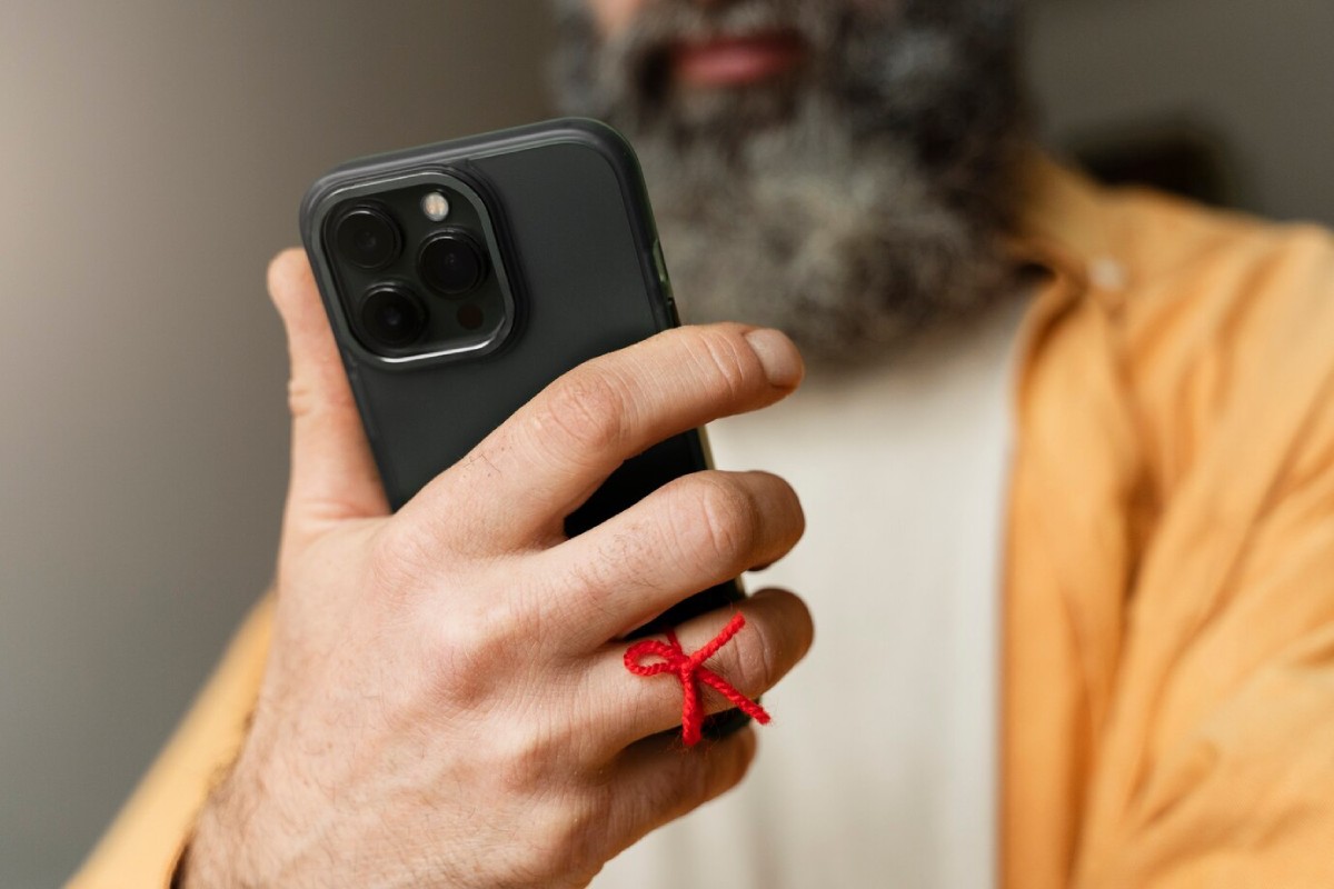 A close-up of a man's hand holding a smartphone, featuring a red string tied around his finger as a reminder.
