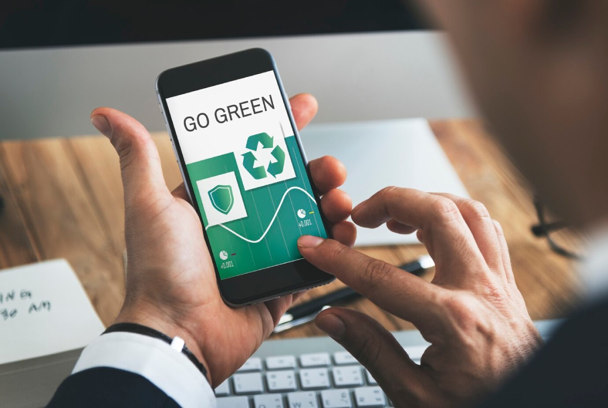 A person holds a smartphone displaying a Go Green eco-friendly app with recycling and growth icons, promoting sustainability.
