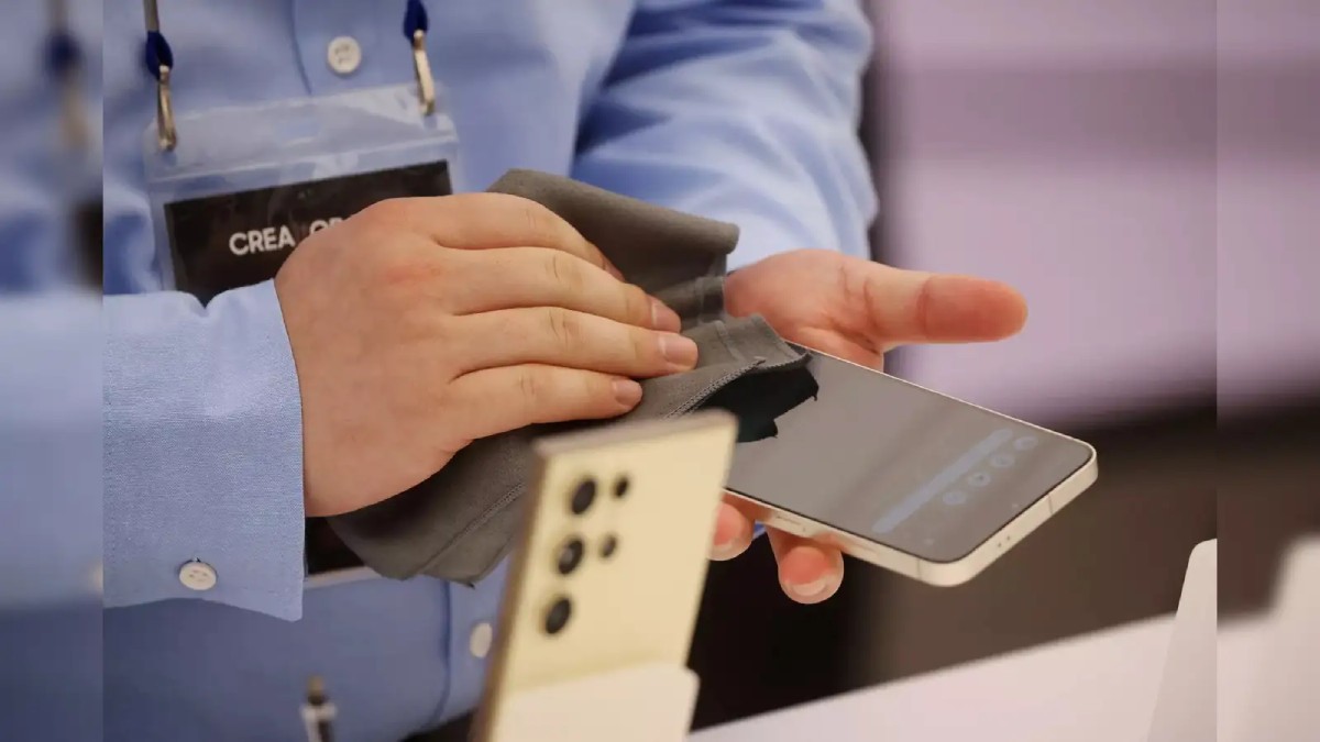 A person in a blue shirt cleans a smartphone screen with a gray cloth at a tech event, showcasing the device's features.