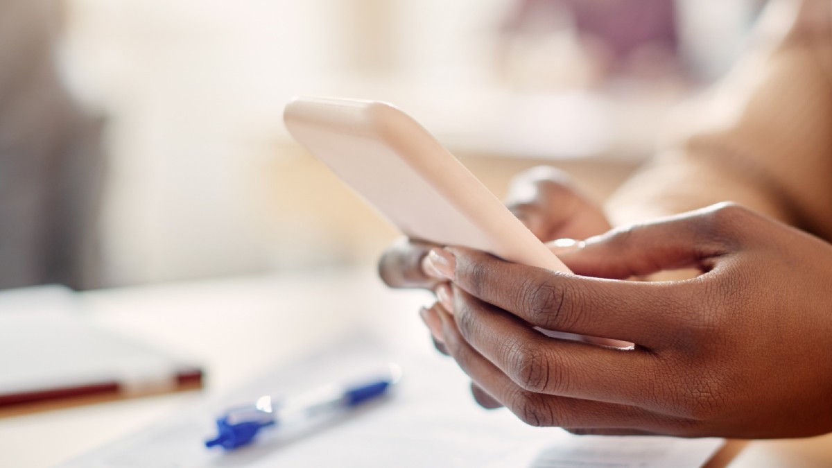 Close-up of a person’s hands holding a smartphone, with a pen and papers in the background, suggesting communication or work.