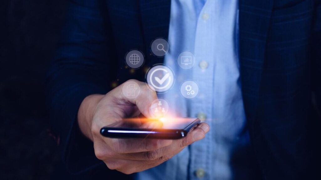 A person in a blue shirt and dark blazer holds a smartphone, with holographic icons representing connectivity and productivity above it.