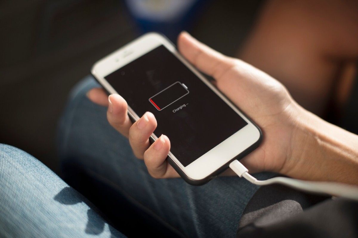 A person holds a smartphone displaying a low battery icon with a charging message, while plugged into a charging cable.
