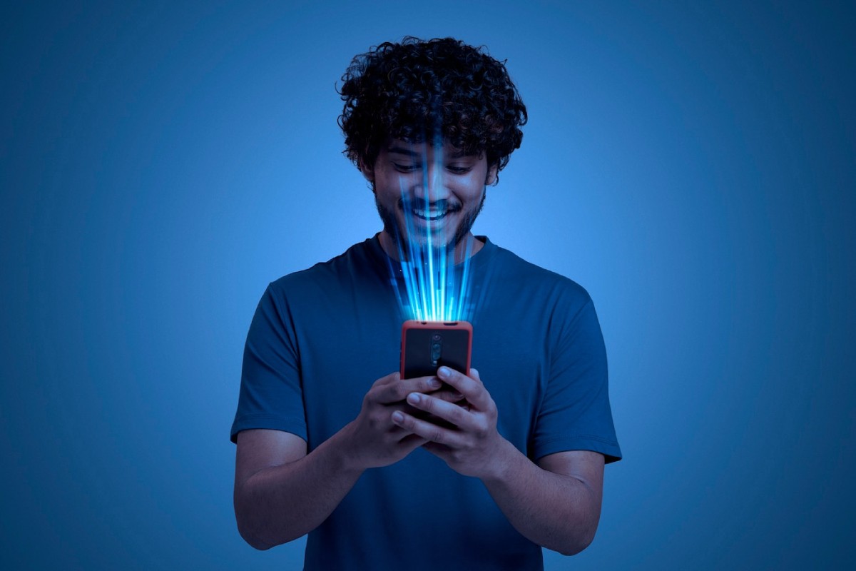 A person in a blue shirt holds a smartphone emitting glowing light beams against a dark blue background.