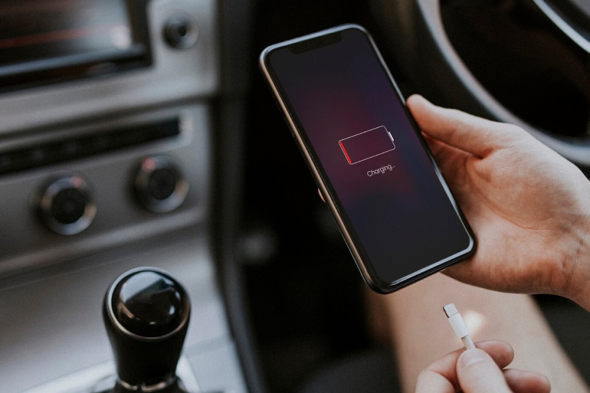A person holds a smartphone displaying a low battery icon with a 