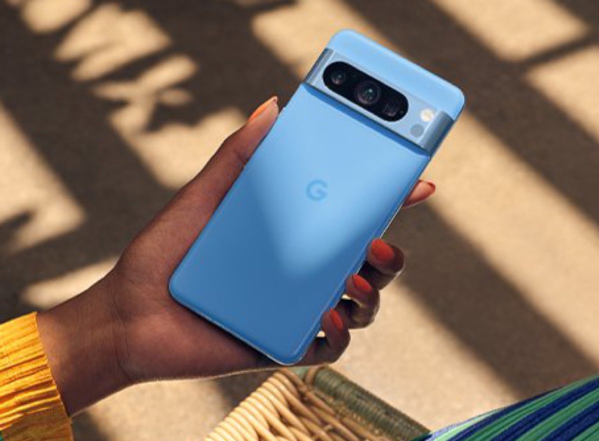 A person holds a pastel blue Google phone, showcasing its sleek design and camera, with sunlight casting shadows in the background.