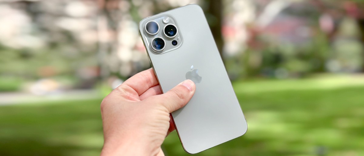 A person holds an Apple iPhone 13 Pro in their hand, showcasing its sleek design against a blurred green background.