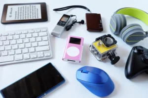 A collection of electronic gadgets including headphones, a smartphone, keyboard, camera, and music player on a white background.
