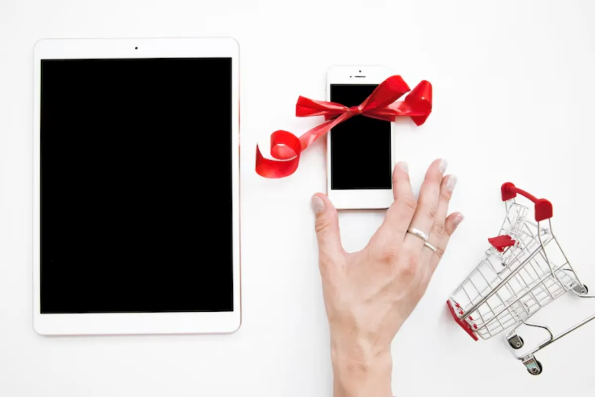 A tablet and a smartphone adorned with a red ribbon, along with a mini shopping cart, on a white background.